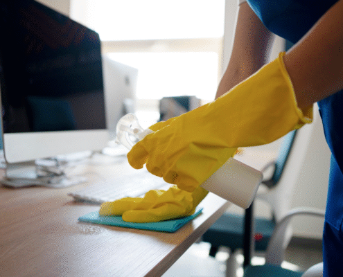 Someone wearing rubber gloves cleaning a desk