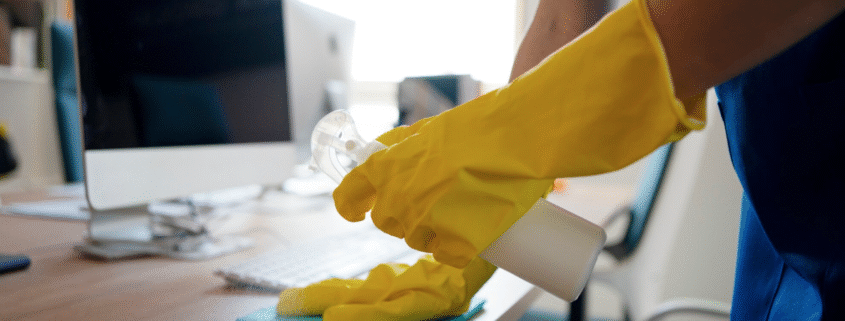 Someone wearing rubber gloves cleaning a desk